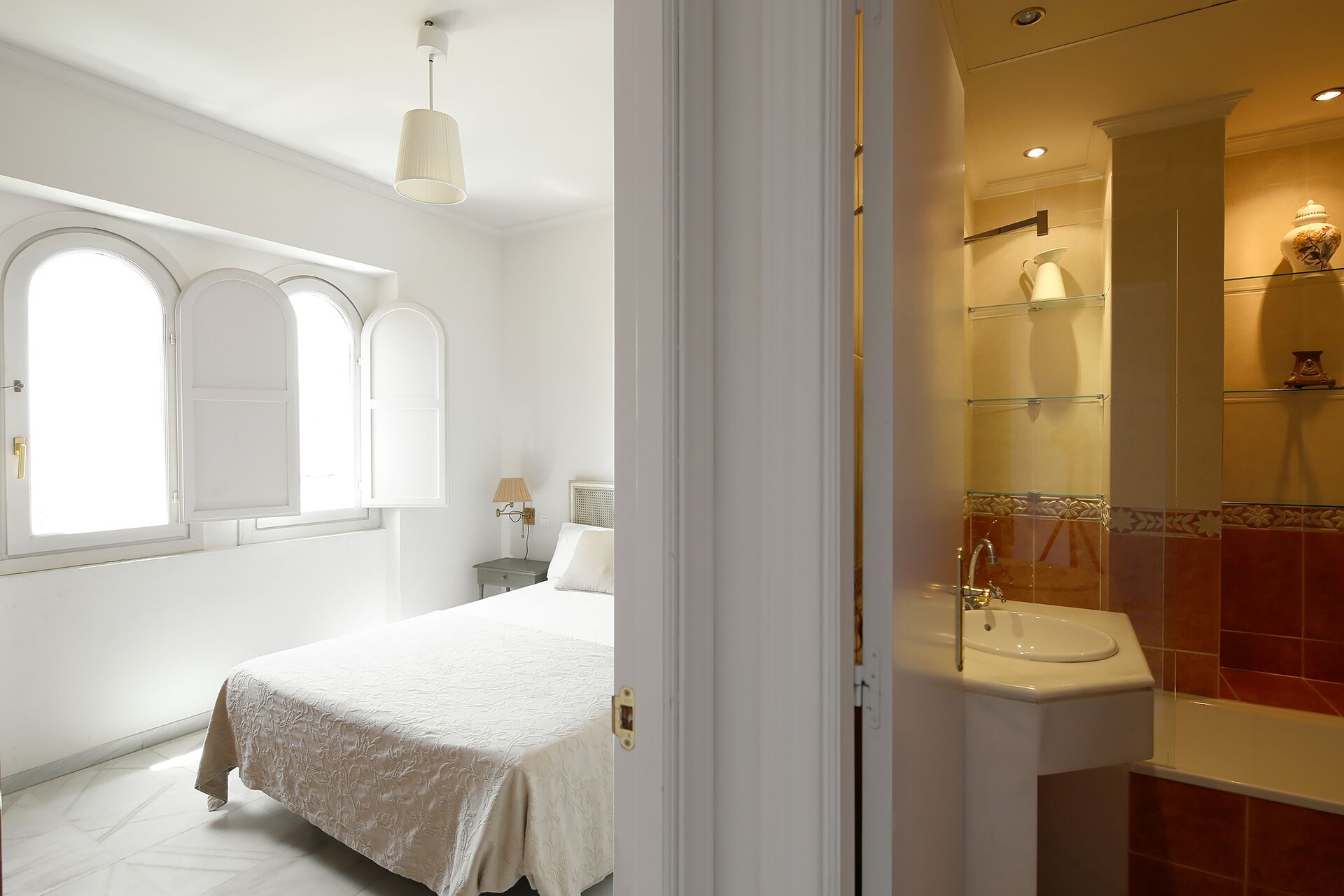 A bedroom with a bed, a nightstand, a lamp, and a window with arched tops.