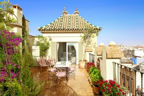 A covered patio with a tiled roof, outdoor seating, and potted plants.