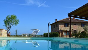 Ein klarer Swimmingpool mit einer Liege, einem Steinhaus und Blick auf die Landschaft.