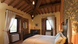 Ein Schlafzimmer mit Bett, Schminktisch, Heizkörper und einer Steinwand.