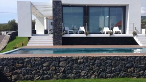 Ein modernes Haus mit Swimmingpool, Steinmauern und einer Terrasse mit weißen Stühlen.