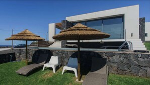 Eine moderne Villa mit Pool, zwei Strohdächern und Liegestühlen.