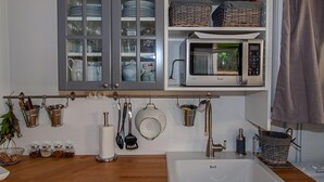 A kitchen with grey cabinets, a microwave, and various utensils hanging on a rack.