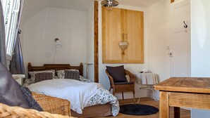 A bedroom with a wooden bed, a wicker chair, a small table, and a wooden wardrobe.