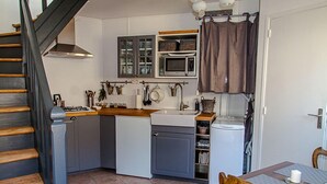 A compact kitchen with a microwave, sink, and cabinets. A staircase leads to another level.