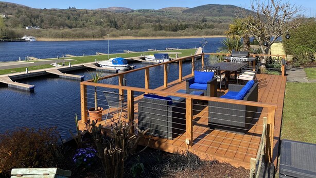 A deck with outdoor seating, a grill, and a view of a lake with boats. - Luxury Riverside Holiday Home in stunning Ballina / Killaloe - The Derg House (Killaloe)