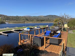 Eine Terrasse mit Sitzgelegenheiten im Freien, einem Grill und Blick auf einen See mit Booten.