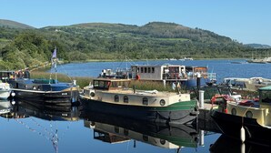 A marina with boats docked, a small building on the dock, and a forested hill in the background. - Luxury Riverside Holiday Home in stunning Ballina / Killaloe - The Derg House (Killaloe)