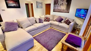 A modern living room with a sectional sofa, a flat-screen TV, and artwork on the walls. - Luxury Riverside Holiday Home in stunning Ballina / Killaloe - The Derg House (Killaloe)