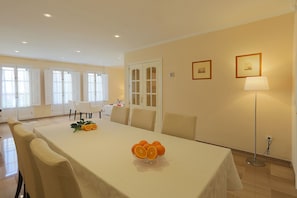 Un comedor con una mesa dispuesta para cuatro personas, un cuenco de naranjas y una lámpara de pie.