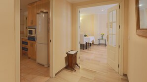 A hallway leading to a dining area with a table set for two, a small cabinet, and a refrigerator.