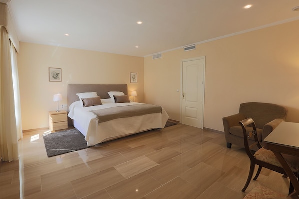 Una habitación de hotel con una cama grande, mesitas de noche, una silla y una puerta.