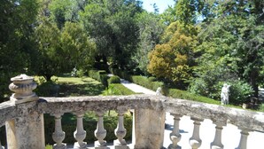 A stone balustrade overlooking a well-manicured garden with various trees and a statue.
