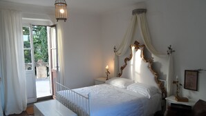 A bedroom with a bed, a bedside table, a nightstand, a chair, a window with curtains, and a hanging light fixture.