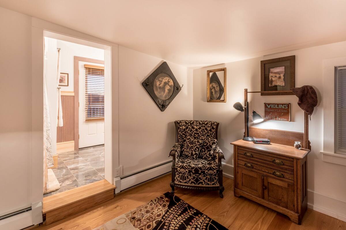 A room with a patterned armchair, a wooden dresser, and a mirror.