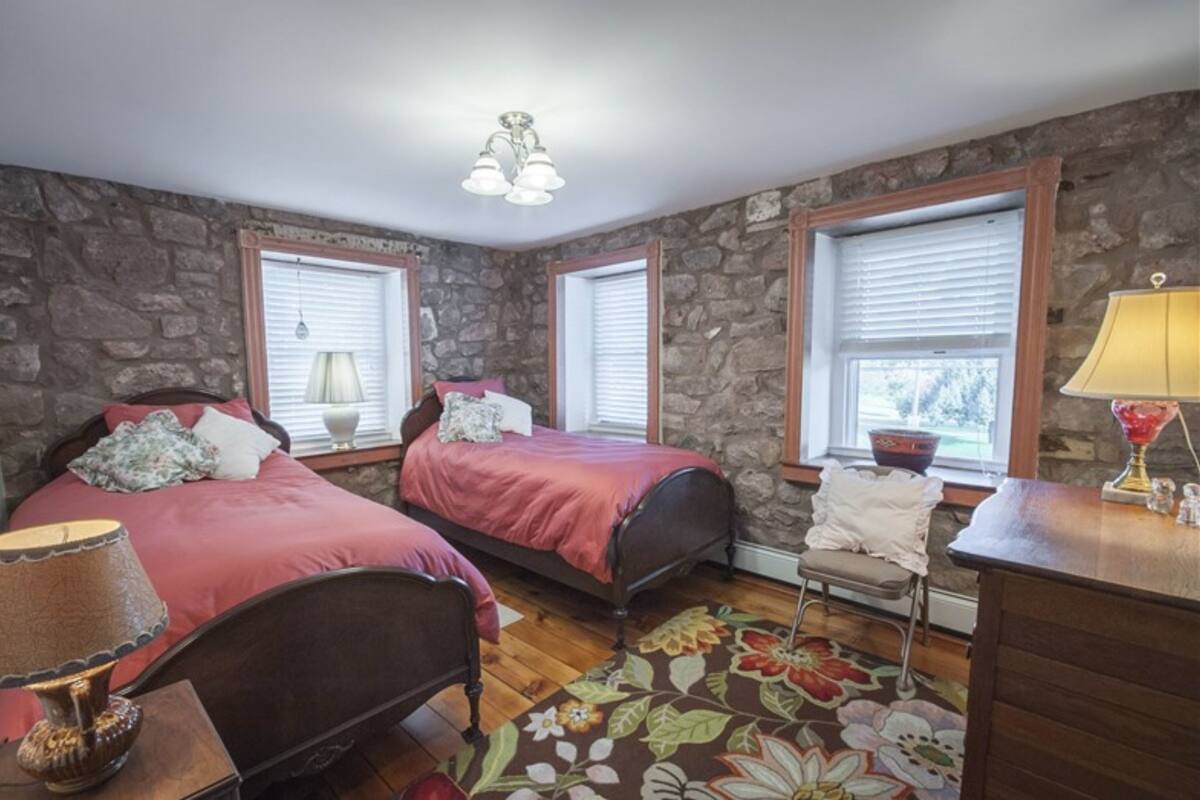 A bedroom with two beds, stone walls, wooden floors, and a desk with a lamp.