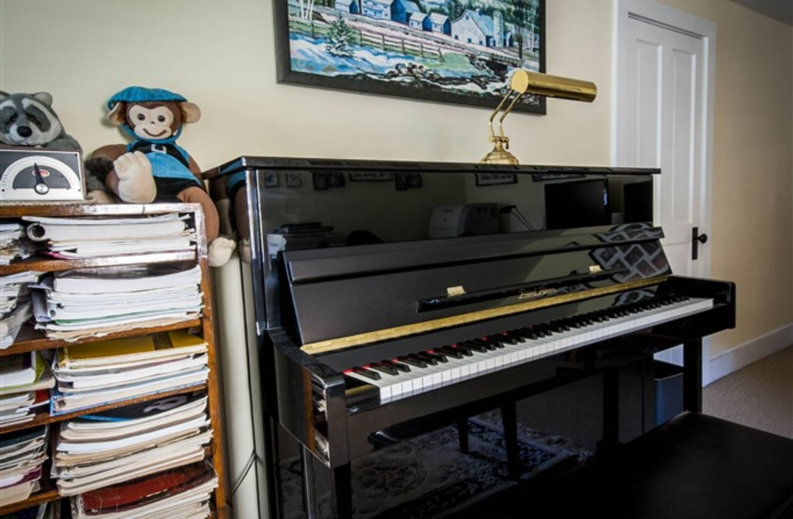 A piano in a room with a bookshelf filled with books and a stuffed monkey toy.