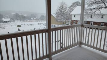A snow-covered balcony with a view of a rural landscape and a building with a white roof.