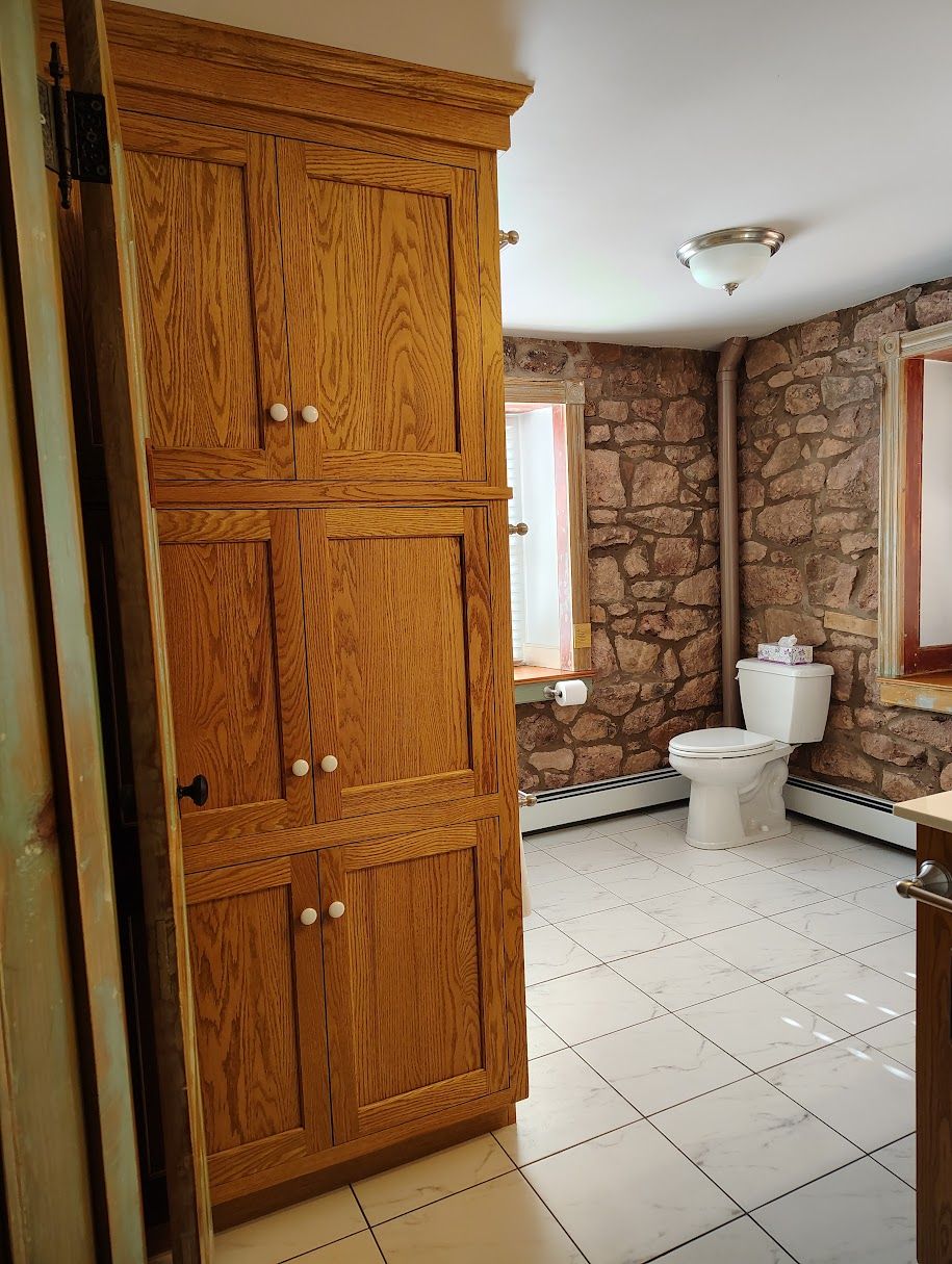 A bathroom with a wooden cabinet, a toilet, and a stone wall.