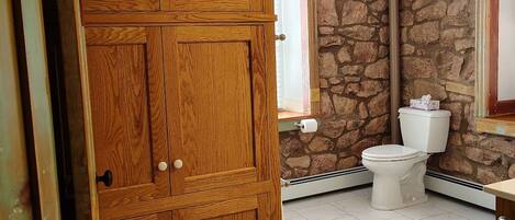 A bathroom with a wooden cabinet, a toilet, and a stone wall.