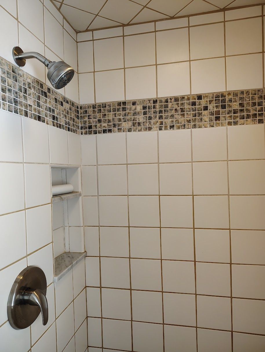A shower area with a tiled wall, a showerhead, and a shelf.