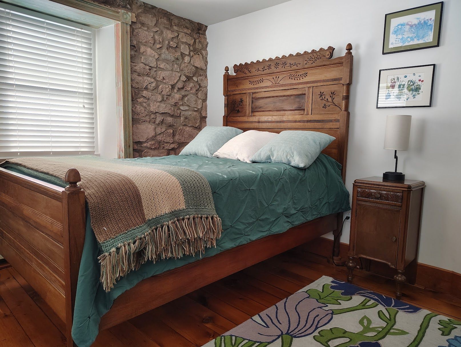 A bedroom with a wooden bed, stone wall, and a nightstand with a lamp.