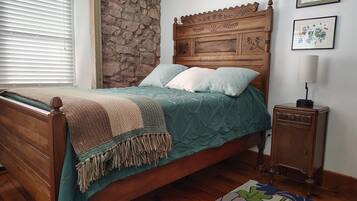 A bedroom with a wooden bed, stone wall, and a nightstand with a lamp.