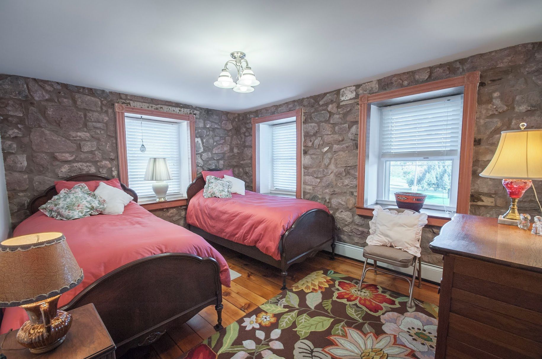 A bedroom with two beds, stone walls, wooden floors, and a floral rug.