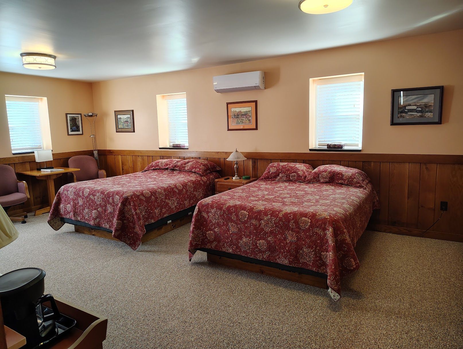 A hotel room with two beds, a desk, a chair, and a coffee maker.