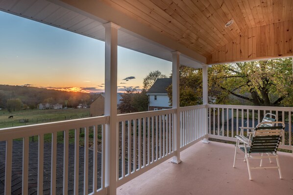 A covered porch with a view of a sunset over a residential area. - Frush Farm Bed & Breakfast (Reinholds)