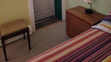 A bedroom with a bed, a bedside table with a lamp, a chair, a door with a window, and a framed picture on the wall.