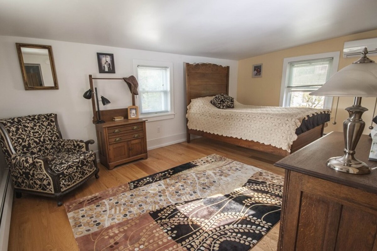 Quarto com cama, poltrona, penteadeira, abajur e tapete.