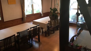Un área de comedor con mesas y sillas de madera, plantas colgantes y un calendario en la pared.