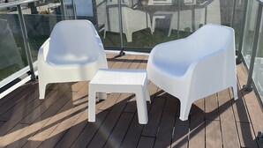Een balkon met twee witte plastic stoelen en een klein tafeltje, met uitzicht op een woonwijk met huizen en een palmboom.