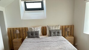 Een slaapkamer met een groot bed, een houten hoofdbord, twee nachtkastjes, een raam en een dakraam.