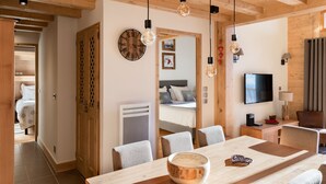 A modern, well-lit room with a wooden ceiling, a dining table with chairs, a bed with a view, and a TV on the wall. - "LES CHARDONS" APARTMENT - 8 Pers - SKI-BY-FOOT - CHAMPAGNY - LA PLAGNE (Champagny-En-Vanoise)