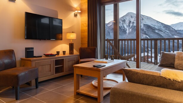 A cozy living room with a TV, wooden furniture, and a balcony with a mountain view. - "LES CHARDONS" APARTMENT - 8 Pers - SKI-BY-FOOT - CHAMPAGNY - LA PLAGNE (Champagny-En-Vanoise)