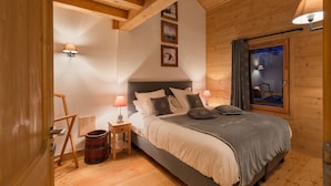 A cozy bedroom with a wooden ceiling, a bed with a grey blanket, two bedside lamps, and a window with curtains. - "LES CHARDONS" APARTMENT - 8 Pers - SKI-BY-FOOT - CHAMPAGNY - LA PLAGNE (Champagny-En-Vanoise)