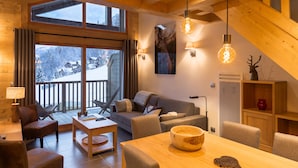 A cozy cabin interior with a wooden dining table, sofa, and chairs, large windows with a snowy view, and a wooden ceiling. - "LES CHARDONS" APARTMENT - 8 Pers - SKI-BY-FOOT - CHAMPAGNY - LA PLAGNE (Champagny-En-Vanoise)