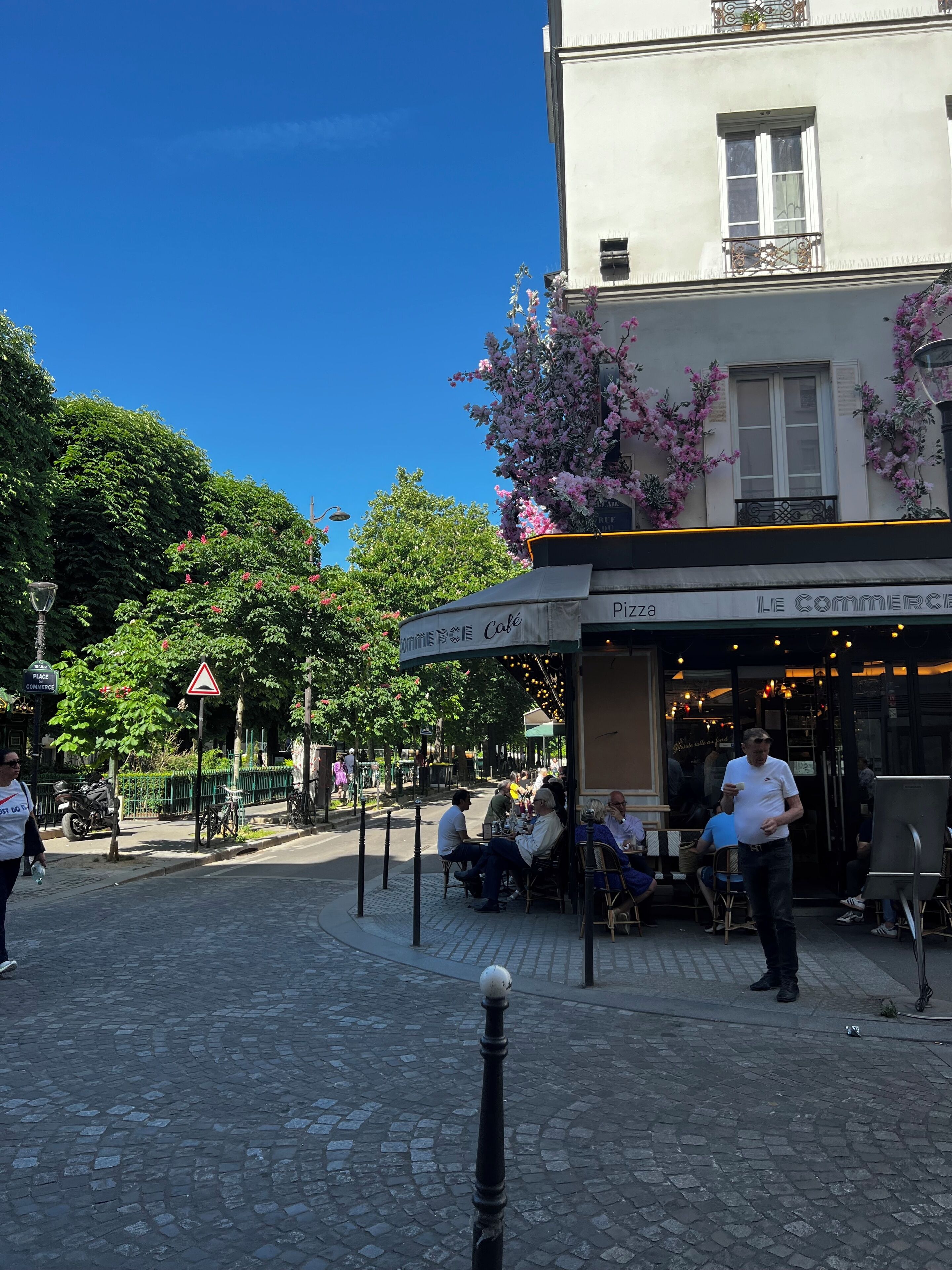 A cobblestone street with outdoor seating at a café named "LE COMMERCIE".