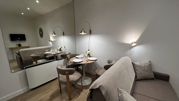 A modern living room with a sofa, a dining table with chairs, a TV mounted on the wall, and a mirror reflecting the room. - Beautiful & quiet flat, ideally located (Paris)