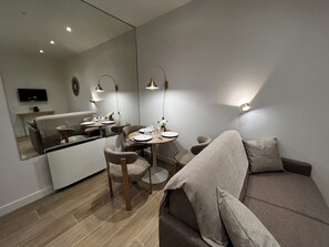 Una sala de estar moderna con un sofá, una mesa de comedor con sillas, un televisor en la pared y un espejo que refleja la habitación.