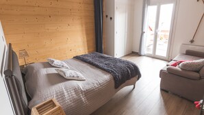 A bedroom with a bed, a sofa, a wooden ceiling, a window, and a door.