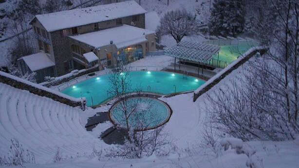 A snow-covered outdoor swimming pool area with a building in the background.
