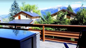 A wooden deck with a table and chairs, overlooking a mountainous landscape with several houses.