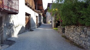 A narrow cobblestone street flanked by traditional stone buildings with wooden balconies and a stone wall on one side.