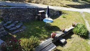 Um muro de pedra, uma mesa pequena com uma cadeira, um banco e plantas em vasos numa área de jardim.