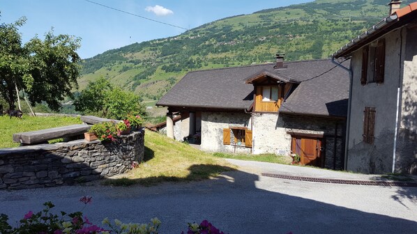 A stone house with a wooden balcony, a stone wall, and a gravel driveway.