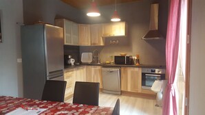 Cozinha compacta com geladeira, micro-ondas, pia e lava-louças. Há uma mesa de jantar com cadeiras e toalha de mesa vermelha.