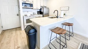 Une cuisine moderne avec des meubles blancs, un îlot central doté de tabourets, un four à micro-ondes et un réfrigérateur.